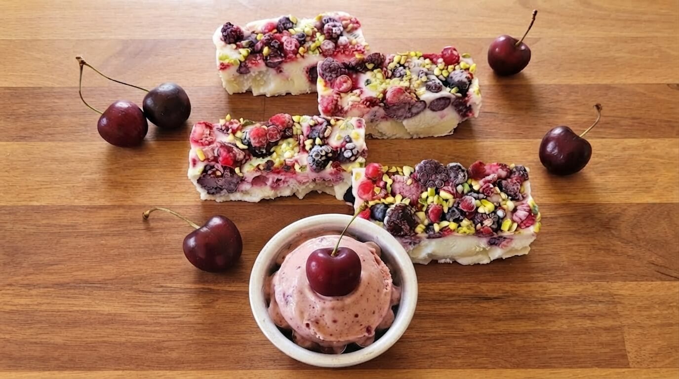 Barrette di yogurt di soia,frutti di bosco e granella di pistacchi e gelato alle ciliegie su tagliere di legno