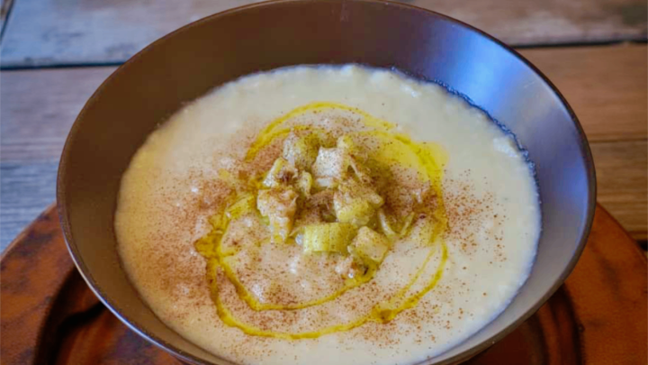 Un piatto di zuppa cremosa servito in una ciotola scura, guarnito con pezzi di verdura e un filo d'olio d'oliva.