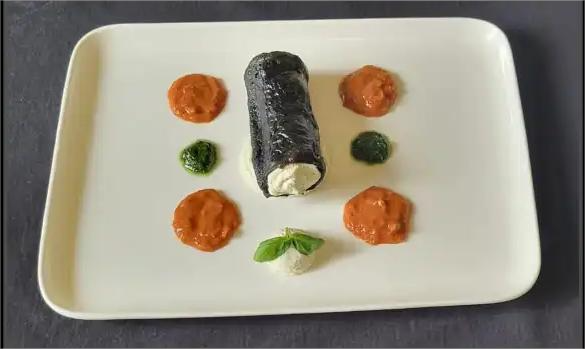 Piatto di antipasto vegano con cannolo di melanzane affumicate, spuma di ricotta, purea di pomodorino e riduzione al basilico, servito su un piatto bianco.