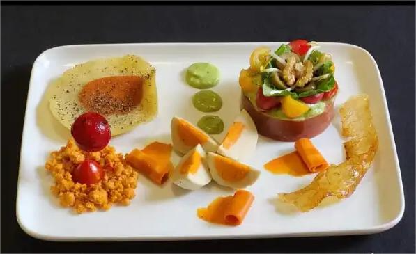 Un piatto gourmet vegano composto da un'insalata di verdure colorate, una salsa verde, pomodorini, e decorazioni artistiche a base di carote e altre preparazioni vegane.