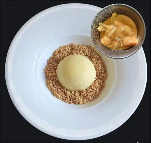 Dessert composto da una sfera di crema con crumble di mandorle e una ciotola con salsa di frutta.