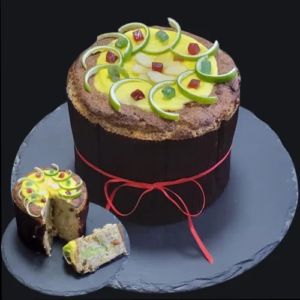 Un dolce festivo decorato con frutta candita e glassa, presentato su un vassoio nero con una fettina tagliata.