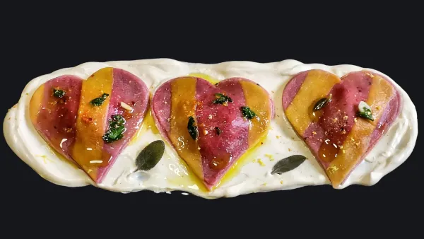 Un elegante piatto gourmet che presenta tre cuori di pasta colorata su una crema bianca, decorato con erbe verdi e un filo d'olio.