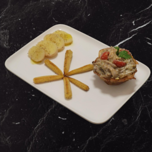 Piatto vegan gourmet con crema di topinambur, pomodorini e contorni di mais baby e fette di patata, servito su un piatto bianco.