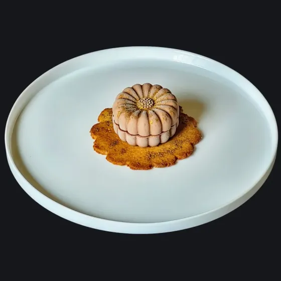 Un dessert vegano gourmet su un piatto bianco, composto da un dolce a forma di fiore color crema su una base di biscotto croccante.
