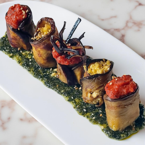 Un piatto di involtini di melanzane farciti con pomodoro e vari ingredienti, serviti su una salsa verde.