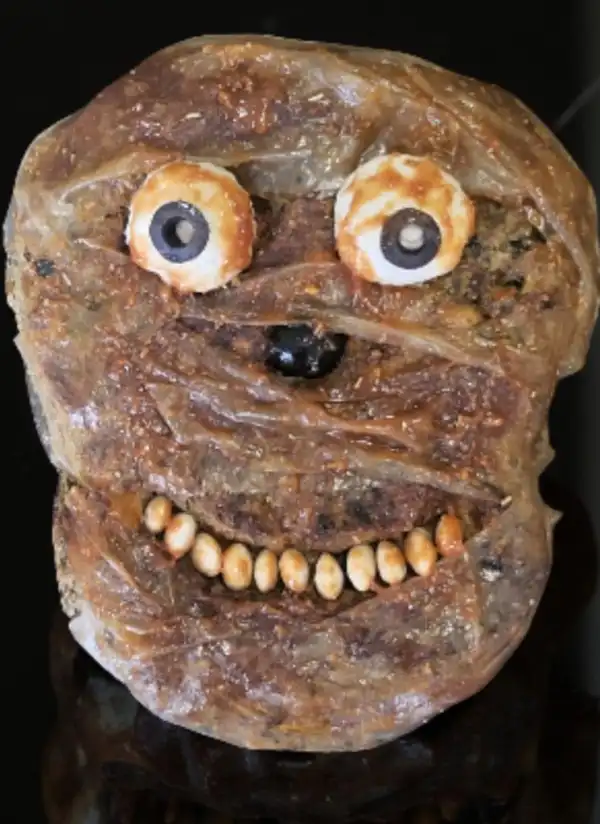 Una creativa preparazione culinaria che assomiglia a un volto sorridente, realizzata con ingredienti vari e decorazioni simpatiche.