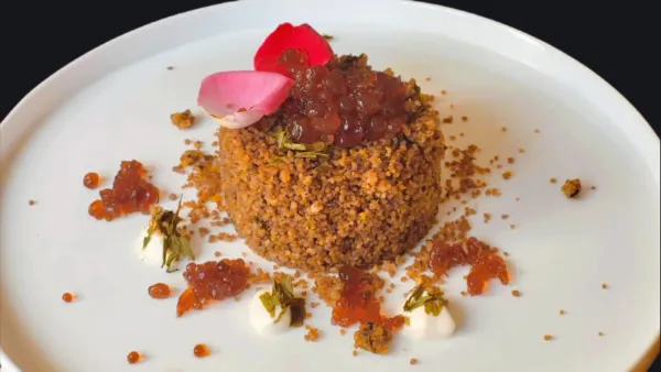 Un piatto di dessert vegano gourmet con una base di granelli, guarnito con gelatina, petali di rosa e crema. Decorato con ingredienti colorati e presentato su un piatto bianco.