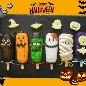 Onigiri spaventosi decorati per Halloween, con forme a gatto, zucca, Frankenstein, scheletro, mummia e tomba di Dracula su uno sfondo colorato.