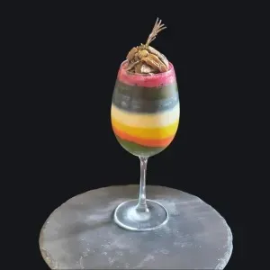 Dessert di frutta fresca gourmet in un bicchiere, con strati colorati di diversi gusti e decorato con un elemento croccante in cima.