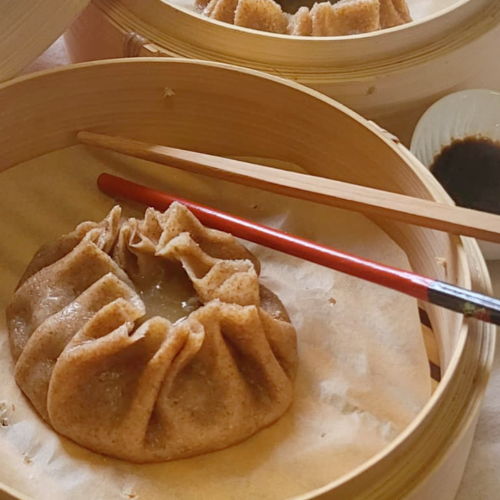 Un dumpling cotto al vapore su carta, con bacchette di legno e salsa di soia accanto.