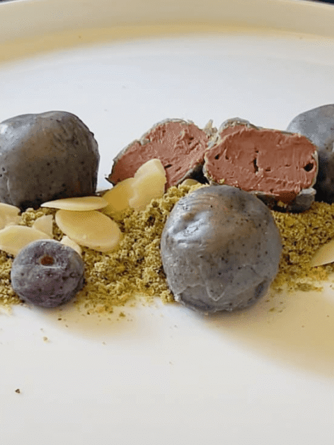 Sfere cioccolattose come sassi su erba di pistacchio,scaglie di mandorle e mirtilli freschi su piatto bianco