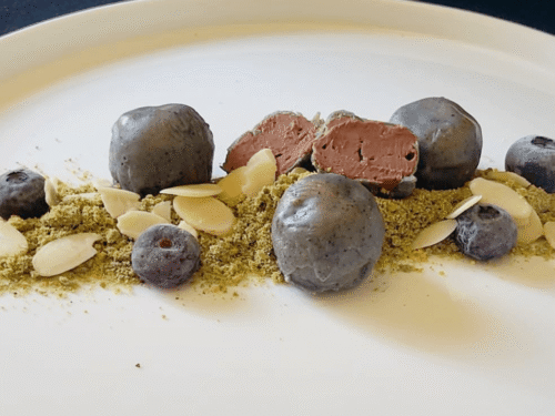 Sfere cioccolattose come sassi su erba di pistacchio,scaglie di mandorle e mirtilli freschi su piatto bianco