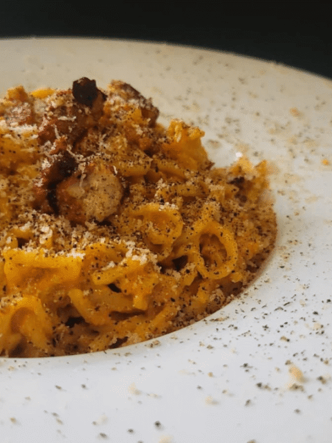 Piatto cappello del prete bianco con tonnarelli con salsa gialla e pezzetti di guanciale : carbonara vegana