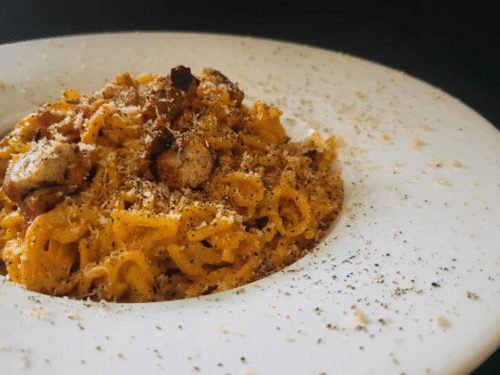 Piatto cappello del prete bianco con tonnarelli con salsa gialla e pezzetti di guanciale : carbonara vegana