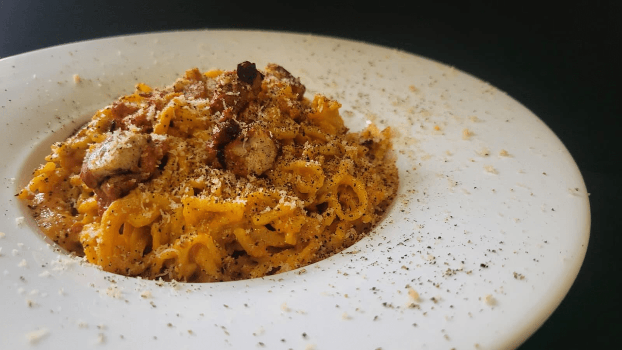 Piatto cappello del prete bianco con tonnarelli con salsa gialla e pezzetti di guanciale : carbonara vegana