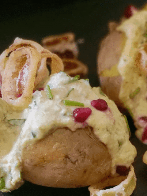 Baked potato ripiena di hummus fave e panna acida su piatto ardesia nero con chicchi di melagrana