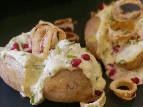Baked potato ripiena di hummus fave e panna acida su piatto ardesia nero con chicchi di melagrana