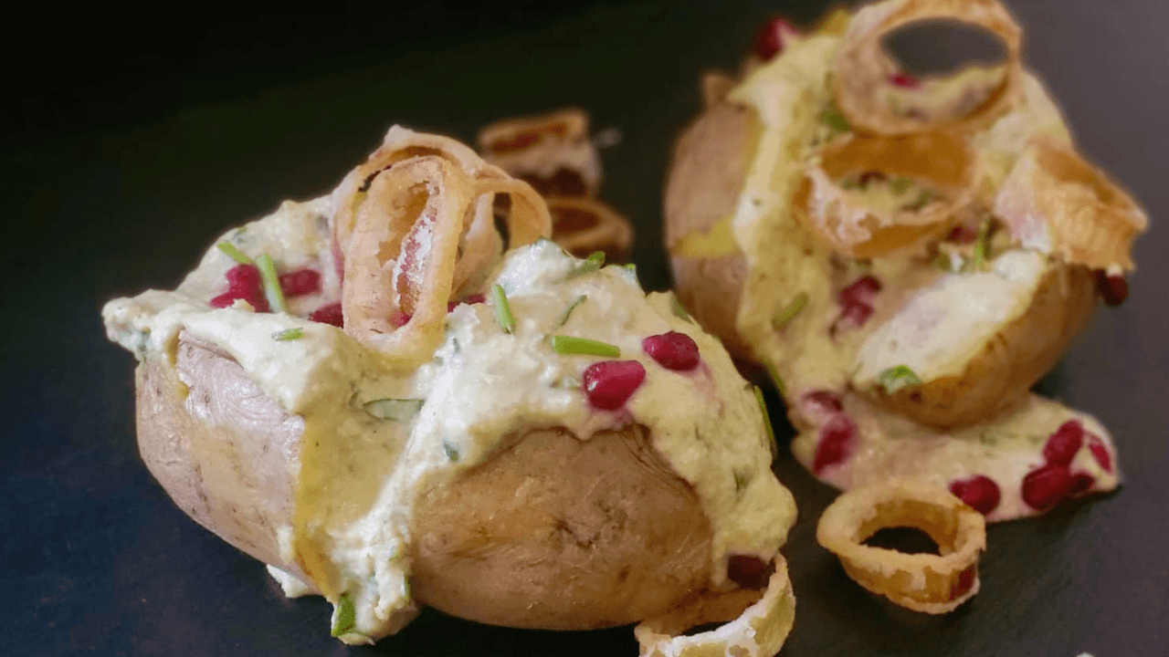 Baked potato ripiena di hummus fave e panna acida su piatto ardesia nero con chicchi di melagrana