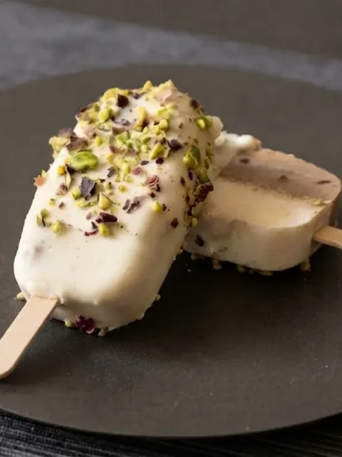 Stecco vegan di semifreddo caffè e mandorla,ricoperto da cioccolato bianco spalmabile al rum su piatto acciaio nero